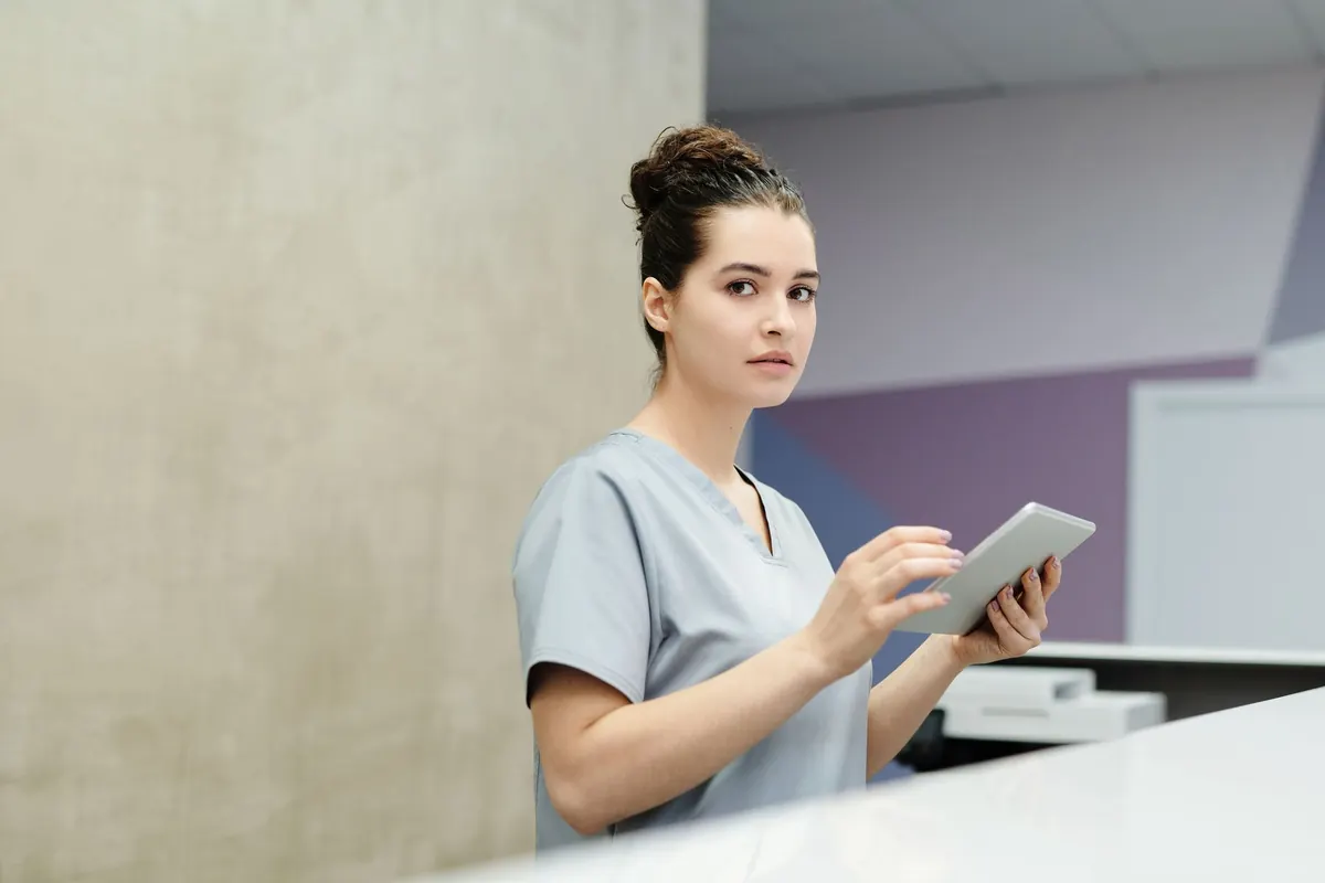 Profesional con uniforme clínico registrando datos en una tablet detrás del mesón de recepción