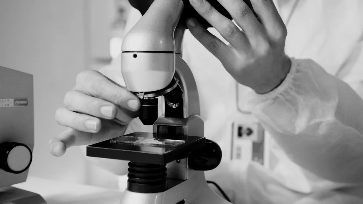 Profesional de laboratorio con delantal blanco ajustando un microscopio para observar una muestra