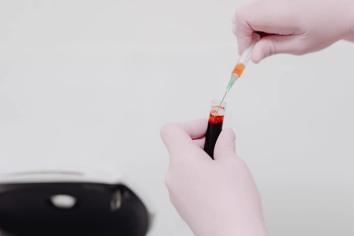 Manos con guantes traspasando una muestra de sangre desde una jeringa a un tubo de laboratorio