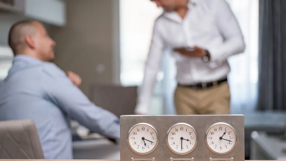 Relojes de pared en una oficina con personas trabajando